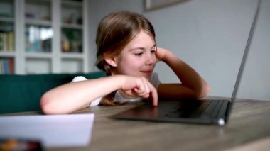 Evde dizüstü bilgisayar kullanan tatlı bir kız. Dikey fotoğraf. Evdeki kız internet üzerinden arkadaşlarıyla iletişim kuruyor. Eğitim, çevrimiçi öğrenim, evde öğrenim, liseli çocuk yaşam tarzı konsepti