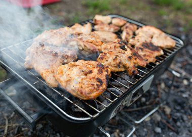 Açık havada portatif kömür mangalında pişen sulu ızgara tavuk butlarının yakın çekimi. Yaz pikniği ya da arka bahçede pişirme konsepti duman ve cızırdayan et. Yüksek kalite fotoğraf