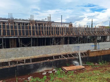 Kısmen inşa edilmiş, beton duvarları ve ahşap iskelesi olan bir bina bulutlu bir gökyüzüne karşı tamamlanmamış bir yapı sergiliyor..