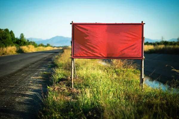 A red billboard sits on the side of a road in a small town.