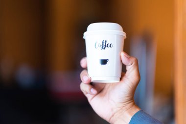 Creamy white coffee mug in male hand with light background.