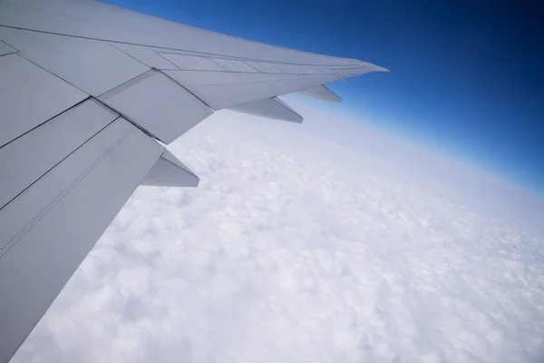 Airplane wing in cloudy sky The plane flies over the beautiful scenery of white fluffy clouds in the blue sky. Air vehicles from a seated person\'s point of view.