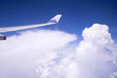 Parlak mavi gökyüzünde bulutların üzerinde uçan uçak kanatları..