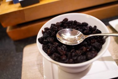 Kuru üzümler beyaz bir bardakta, üstünde kepçeyle. Masada yemeye hazır mısın?.