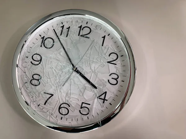 Clock with cracked and broken glass on creamy white background.