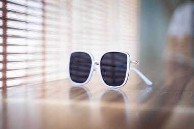 Masanın üzerinde beyaz çerçeveli güneş gözlüğü var. Sabah Bokeh hafif arkaplan.