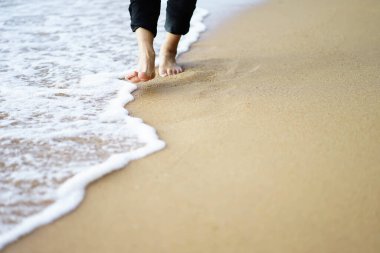 Deniz dalgalarıyla sahilde yürüyen erkek bacakları..