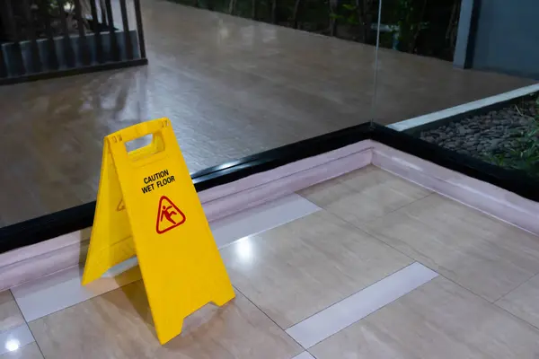 Yellow signs on the floor mark the area being cleaned. The floor is wet, be careful it\'s slippery.