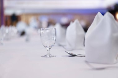 Geleneksel yuvarlak şekilli berrak bir şarap kadehinin yakın çekimi. Mutfak malzemelerinin olduğu beyaz bir yemek masasında restoranın bulanık bir arka planı var..