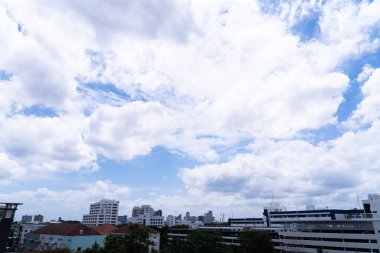 Açık bir yaz gününde gökdelenlerin üzerinde süzülen beyaz bulutlu mavi gökyüzü.