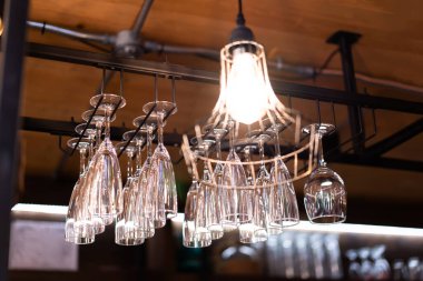 Temiz, yıkanmış ve cilalanmış bardaklar bar raflarında asılı, bulanık arka plan.