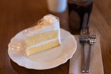 Beyaz bir tabakta hindistan cevizli kek bir fırında ya da kahve dükkanında ahşap bir masada..