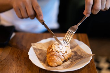 Man eating croissants at wooden table in restaurant. Close-up of cut croissants on plate. clipart