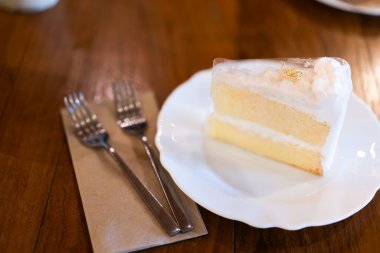 Beyaz bir tabakta hindistan cevizli kek bir fırında ya da kahve dükkanında ahşap bir masada..