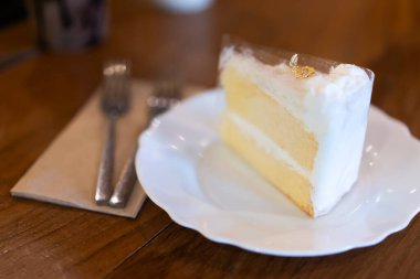 Beyaz bir tabakta hindistan cevizli kek bir fırında ya da kahve dükkanında ahşap bir masada..