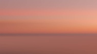 Sakin bir okyanusun üzerine yansıyan ılık pembe-turuncu renk tonlarıyla sakin bir günbatımı. Açık havada barışçıl bir ufuk oluşturmak için doğa sahneleri ve arka planlar için idealdir.
