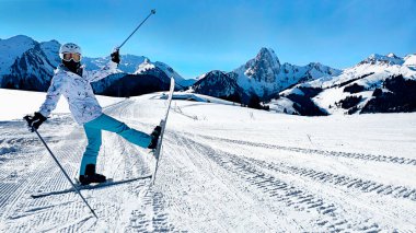Neşeli bir kayakçı arka planda görkemli dağlarla karlı bir kayak pistinde poz veriyor..