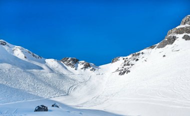 Mükemmel hazırlanmış kayak izleri açık mavi gökyüzünün altında karlı Alp yamaçlarında dönüyor..