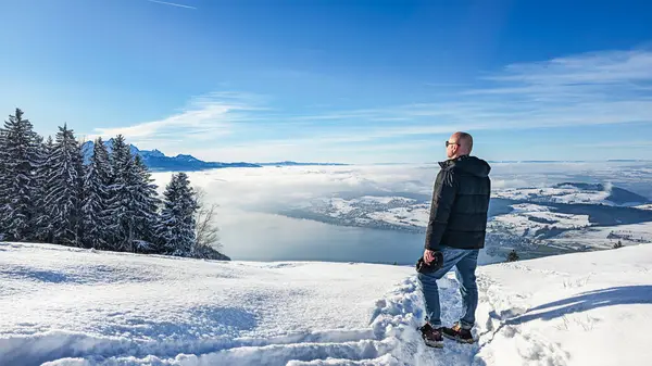 Karlı arazide duran bir adam, bir kış vadisi ve dağların panoramik manzarasının tadını çıkarıyor..
