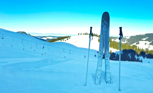 Yoğun bir kayak merkezi manzaralı, karlı bir yamaçta bir çift kayak ve sırık..