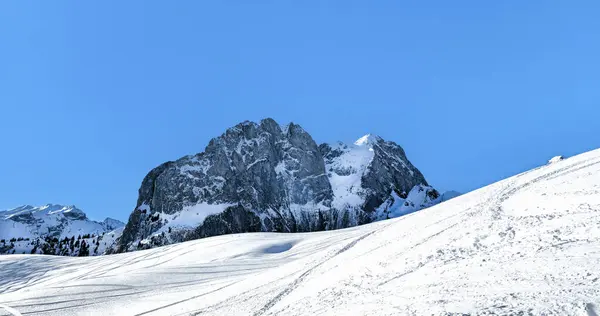Görkemli karlı dağ zirveleri açık mavi gökyüzünün altında beyaz yamaçların üzerinde yükseliyor..