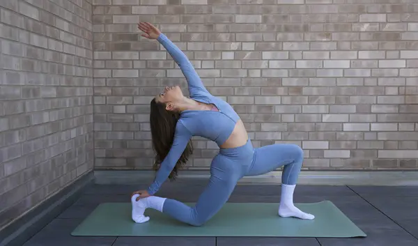 Bir kadın, çatıdaki bir paspasın üzerinde yoga pozu veriyor. Güneş batıyor, incelikle esnedikçe esnekliğini vurguluyor..