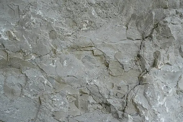Kalıplı gri taştan bir duvarın yakın çekimi. Yüzeyde doğal jeolojik desenleri gösteren renk farklılıkları ve çatlaklar var. Arkaplan ya da inşaat temaları için ideal.