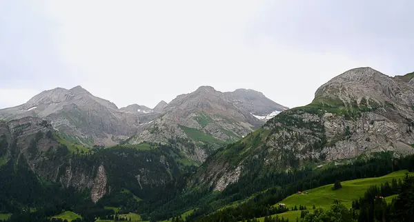 Çarpıcı dağ manzaraları, yüksek tepeler ve yemyeşil vadiler, dramatik bir gökyüzü ile çevrili, doğal çevrenin sakin atmosferini vurguluyor.