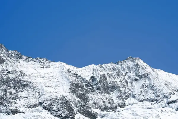 Snow-capped mountain peaks tower against a vibrant blue sky, highlighting the stunning natural beauty and tranquility of the alpine landscape
