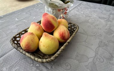 Masadaki küçük hasır sepetin içinde taze şeftaliler.