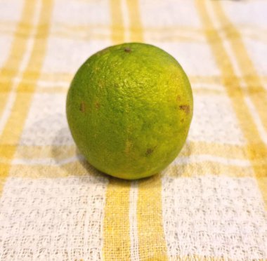 Sarı çizgili beyaz bulaşık havlusunda küçük yeşil limon.