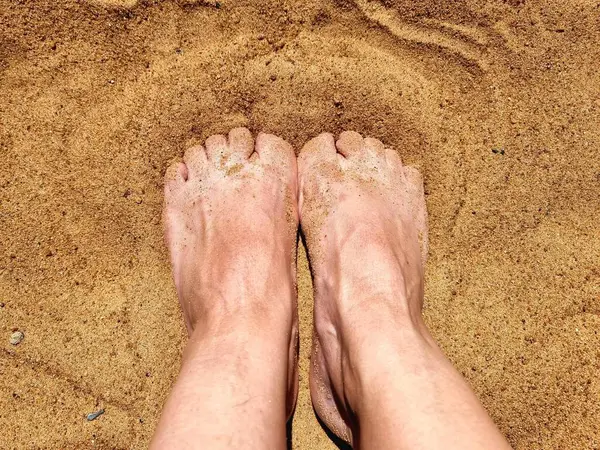 Ayakları kumsalda kuma sıkışmış beyaz bir insanın 60 cm 'si. Fotoğraf ayak bileklerinin bir kısmını gösteriyor..