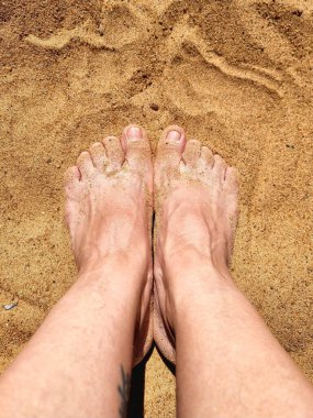 İki beyaz insan ayağının kumsalda çekilmiş fotoğrafı ayak bileklerinin, ayak parmaklarının ve kenarlarının kumla kaplı olduğunu gösteriyor..