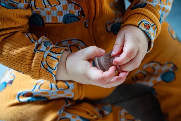 Küçük bir çocuğun elleri emzik tutarken, turuncu bir elbise içinde, neşeli bir araba deseninde..