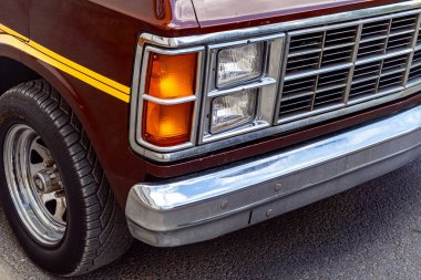 Turuncu sinyal lambası, krom ızgara, tampon ve ön tekerleğin detaylı yansımalarını gösteren klasik bir minibüsün önü..