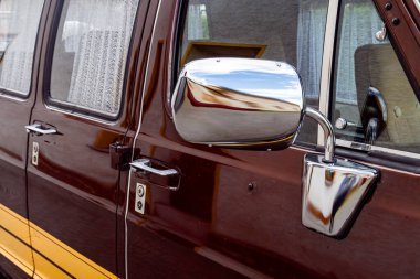 Parlak krom yan aynaları, sapları ve dantel perdeli pencereleri gösteren, kentsel çevreyi yansıtan eski bir minibüsün yakın çekimi..