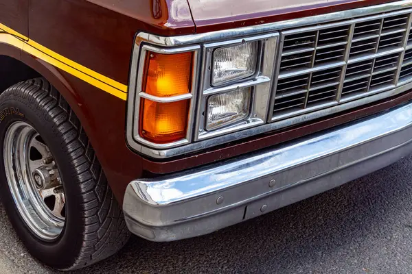 Turuncu sinyal lambası, krom ızgara, tampon ve ön tekerleğin detaylı yansımalarını gösteren klasik bir minibüsün önü..