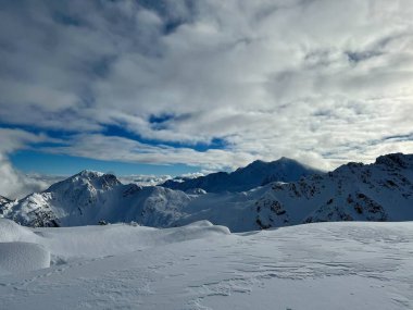 A stunning alpine scene of snow-covered peaks beneath a sky filled with scattered clouds. The untouched snow and rugged mountain terrain create a striking contrast, capturing the essence of winters raw and pristine beauty. clipart