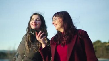 İki arkadaş gölün kenarındaki akıllı telefondan bir şey izlerken bir anlık kahkaha atmanın keyfini çıkarıyorlar.