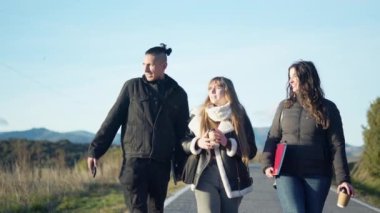 Öğrenciler kahve içip güneşli bir yolda yürürken ödevlerini tartışıyorlar.