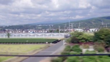 Japonya 'daki yüksek hızlı trenden yakalanan elektrik direkleri, dağ manzaraları ve tarım su rezervleriyle hareket eden yeşil peyzaj. Yüksek kalite 4k görüntü