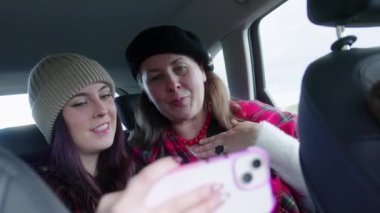 Kış kıyafetli iki kadın arka koltuktaki selfie için gülümsüyor ve poz veriyor. Yüksek kalite 4k görüntü