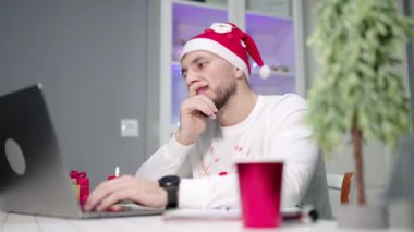Noel Baba Şapkası ve Smartwatch Giyen Genç Profesyonel Daktilo, Bulanık Noel Ağacı, Bayram Işıkları ve Kırmızı Kupa ile çevrili. Yüksek kalite 4k görüntü