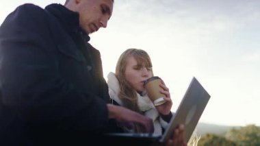 Laptop kullanan ve dışarıda kahve içen genç profesyoneller.