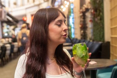 Genç bir kadın şık bir barda ferahlatıcı bir mojito kokteyli içiyor.