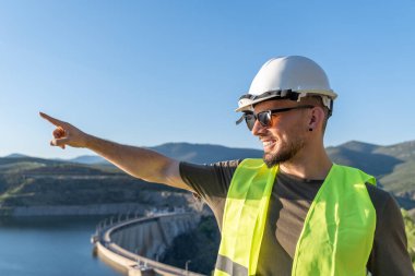 Güvenlik yeleği ve miğfer takan kalite denetleyiciler teftiş sırasında barajı işaret ederek yapısal bütünlük ve operasyonel verimliliği sağlıyorlar.