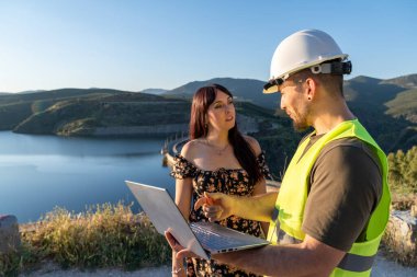 İki mühendis, barajın yakınındaki bir dizüstü bilgisayarla bir projeyi tartışıyorlar.