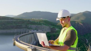 Hidroelektrik barajında çalışan profesyonel mühendis, dizüstü bilgisayarla güç üretimini uzaktan yönetiyor, yenilenebilir enerji altyapısını dijital teknolojiyle izliyor.