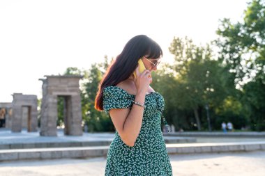 Madrid 'de güneşli bir yaz gününde İspanya' ya hediye edilen eski bir Mısır tapınağı olan debod tapınağında akıllı telefonunu kullanan genç bir kadın.