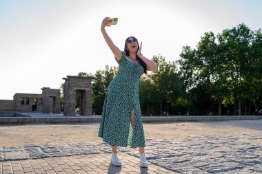 Genç bir kadın güneşli bir yaz gününde Madrid, İspanya 'daki debod tapınağında akıllı telefonuyla selfie çekiyor.